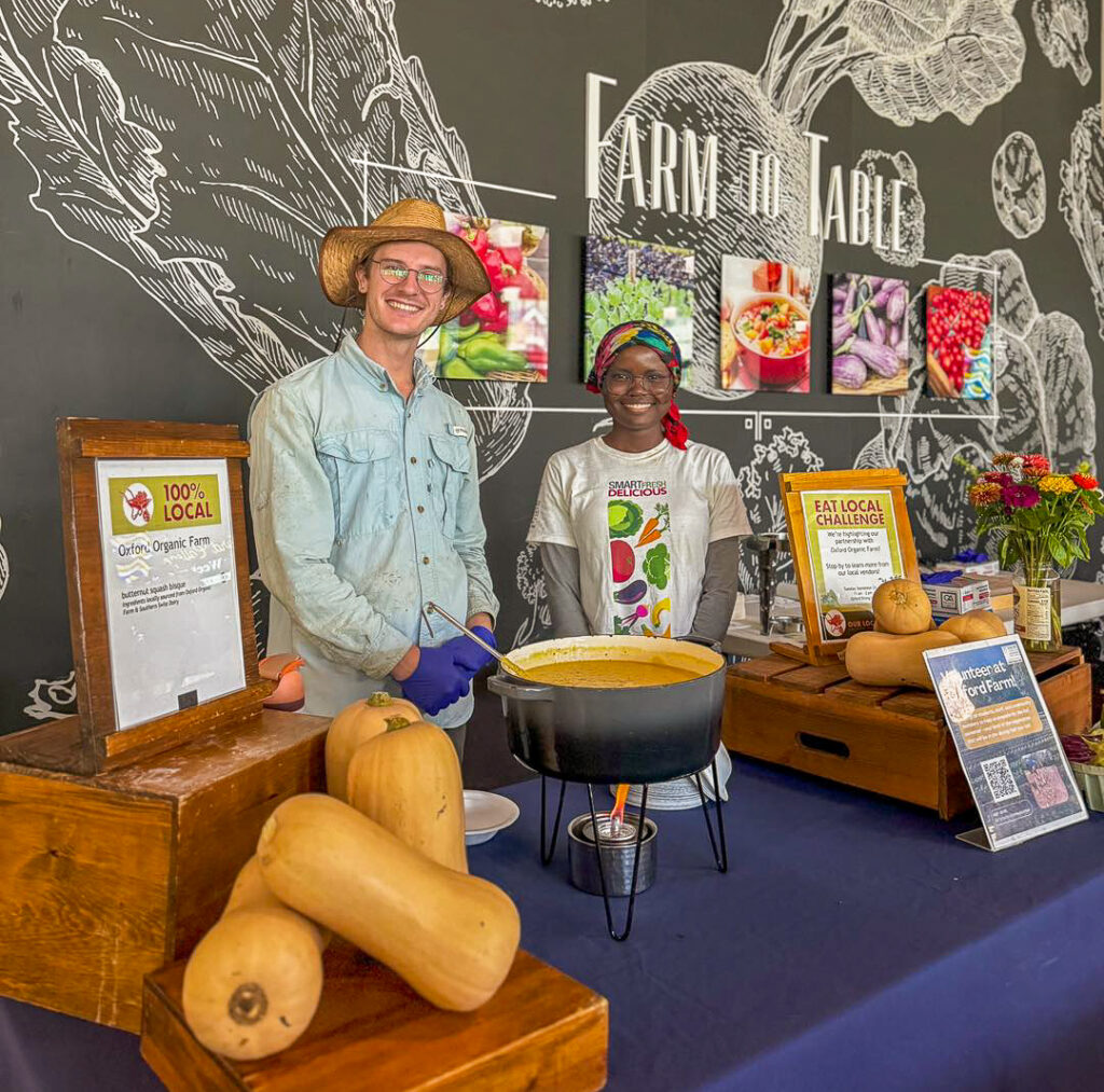A man in a hat and a woman in a headscarf stand behind a farm to table display.
