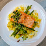 A beautiful piece of pink steelhead trout over green beans, corn, and other vegetables.