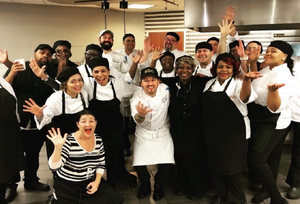 A group of culinary professionals pose for a shot in a commercial kitchen