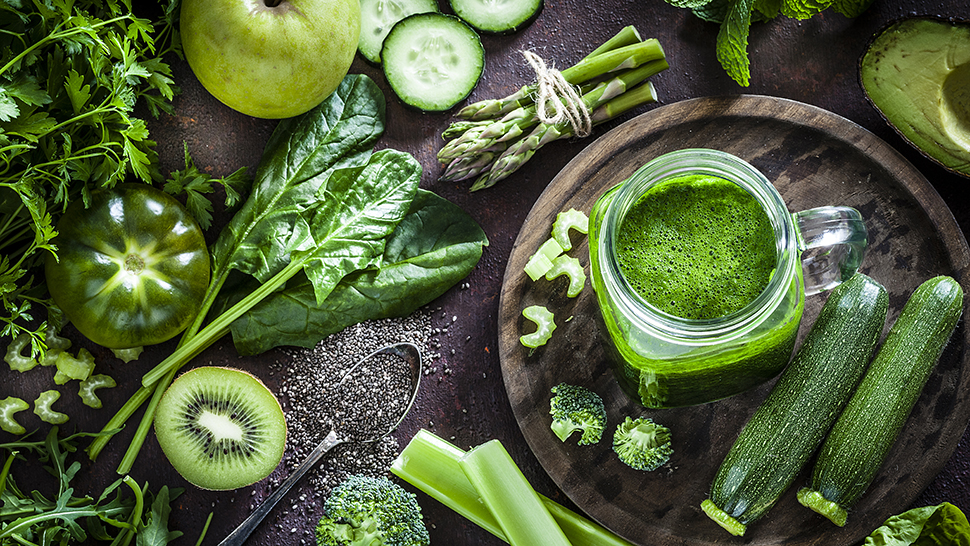 Top view of a rustic table filled with green fruits and vegetables for a perfect detox diet. At the left of an horizontal frame is a glass with fresh green smoothie and a large variety of fruits and vegetables are all around it. Predominant color is green. Low key DSRL studio photo taken with Canon EOS 5D Mk II and Canon EF 100mm f/2.8L Macro IS USM