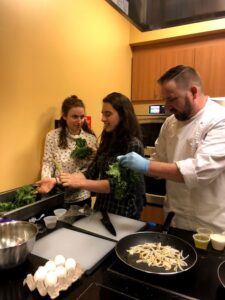 Then an Emory student, Elise (center) de-stems kale for an African squash and kale frittata during a 2018 plant-based cooking demonstration