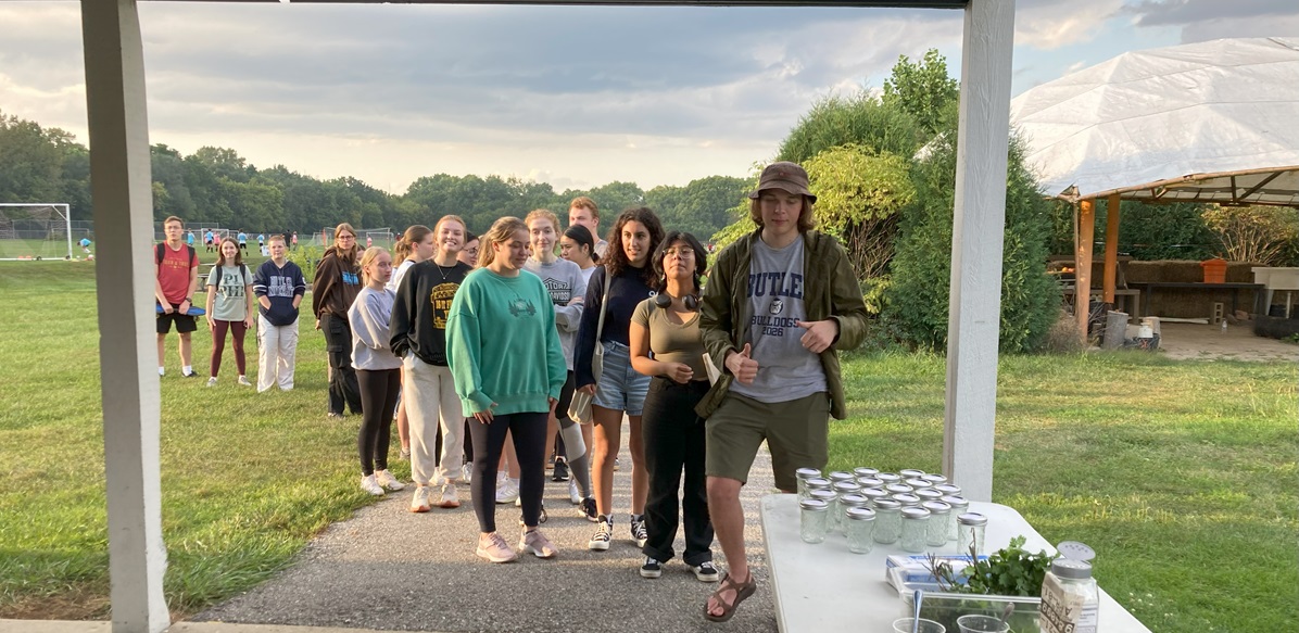 A line of people on a farm approaches a table set up for a demonstration.